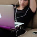 Girl sitting on couch with her headphones in staring at laptop screen disconnected from community.